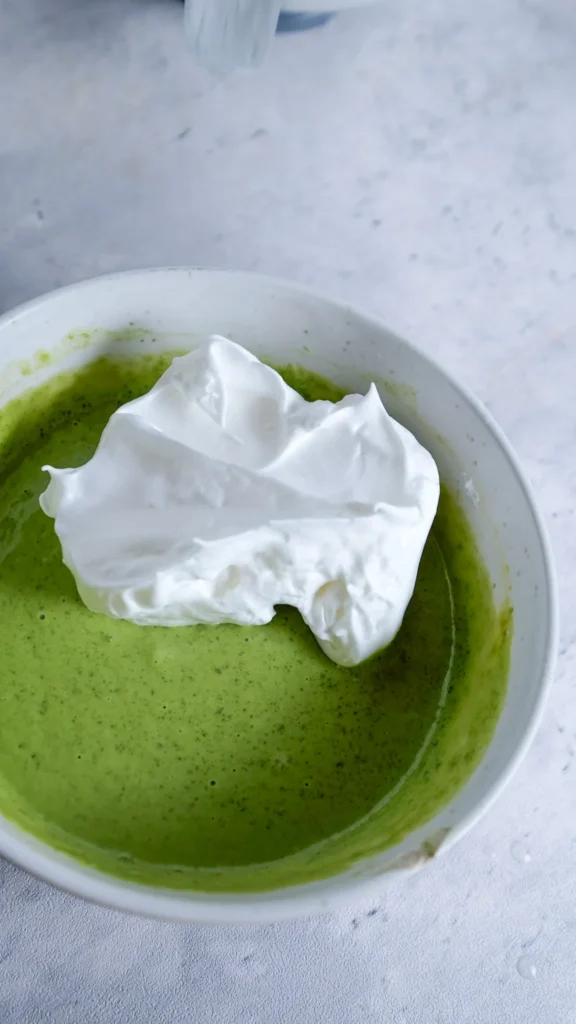 stiff peak egg whites are in a white bowl with the matcha mixture 